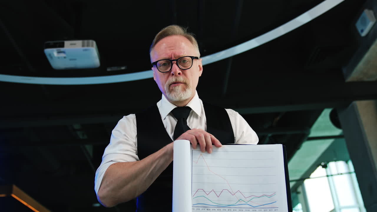 Bearded Caucasian male in shirt, vest and tie shows the papers. Smiling man displays the chart. Low angle view.
