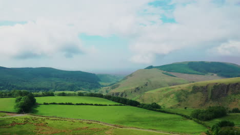 Aerial-rising-shot-over-fields-surrounded-by-mountain-in-the-English-Lake-District,-bright-sunny-day