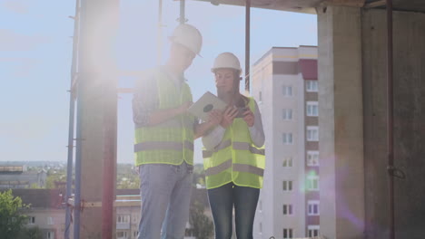 business building teamwork technology and people concept - smiling builders in hardhats with tablet pc computer outdoors