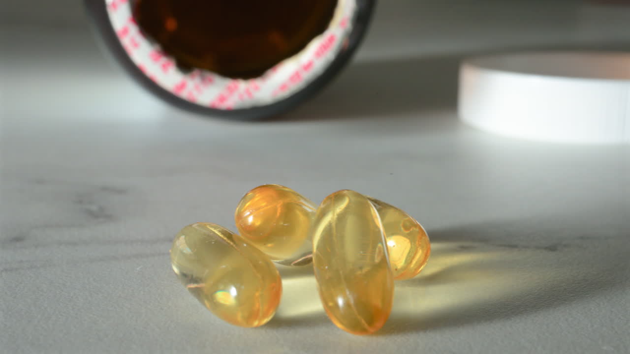 Close up of fish oil supplements scattered on a white table near a pill bottle