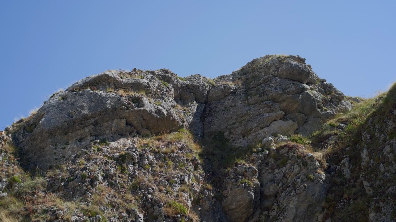 Cima di scogliera calcarea rocciosa contro un cielo azzurro limpido. Ripresa panoramica a mano libera dal basso verso destra di una formazione rocciosa montuosa e aspra in estate