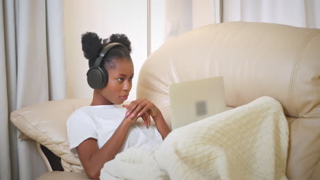 woman relaxing on couch with laptop and headphones