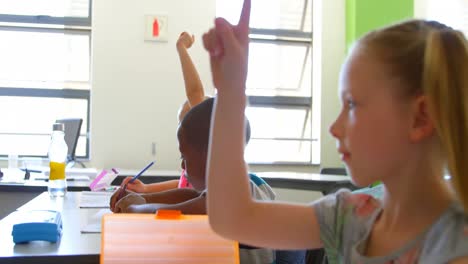 schoolgirl sitting at desk and raising hand in classroom at school 4k