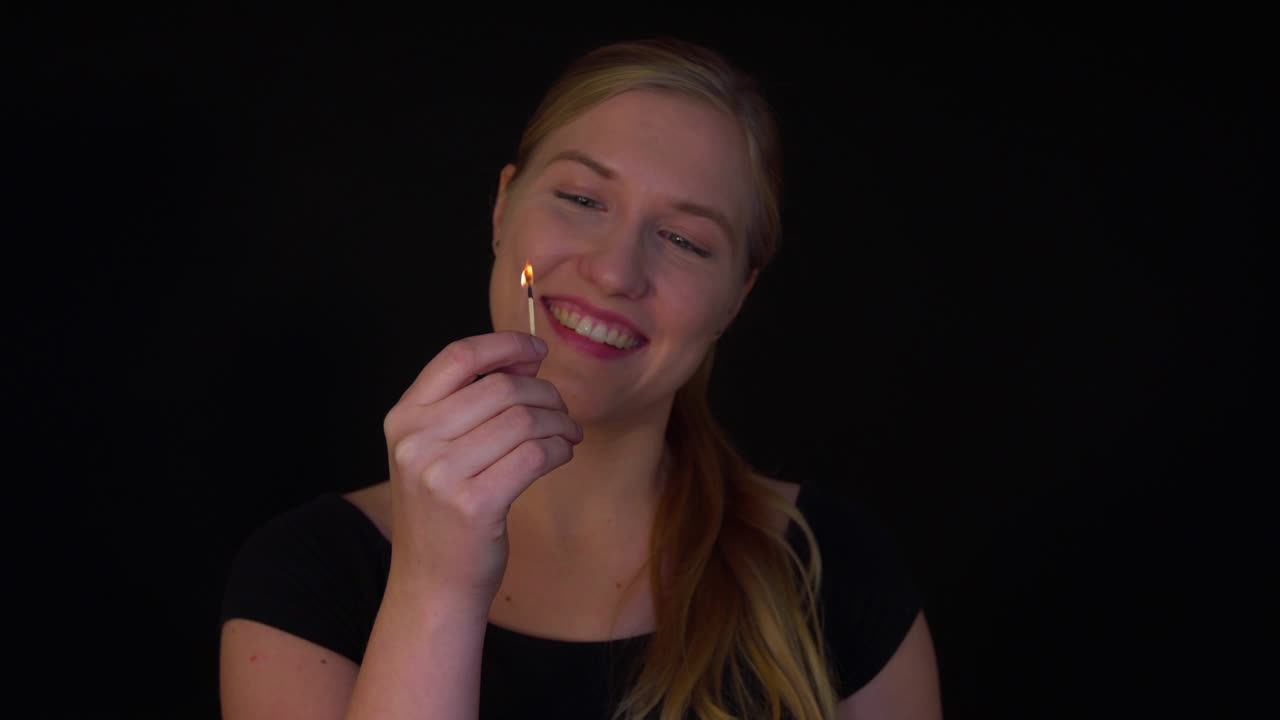 Arsonist woman. A young pyromaniac holds a lit match in her hand and smiles. A dangerous flame in the hands of a crazy woman