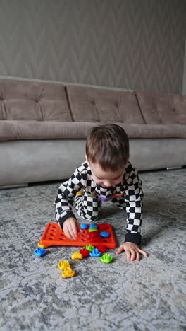 lovely baby boy wearing black and white pajama plays on the floor with a toy. cute child having fun at home. vertical video.
