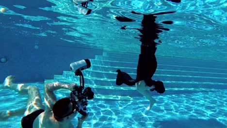 a beautiful blonde girl in a black dress dives under the water to the bottom of the pool, and a man photographer swims under the water and shoots her on a professional underwater camera. slow motion.