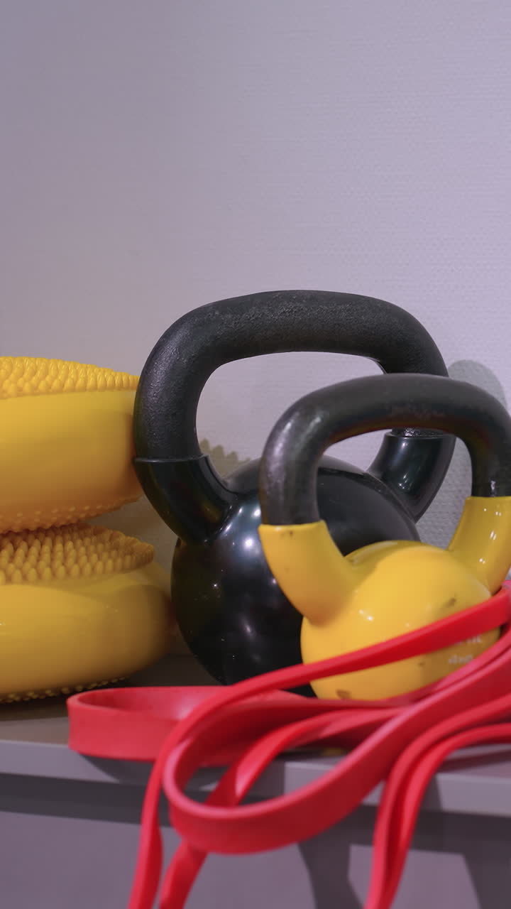 primo piano di varie attrezzature da palestra, comprese kettlebell, bande di resistenza e dischi di equilibrio, ben disposti su uno scaffale, creando uno spazio di allenamento organizzato e funzionale
