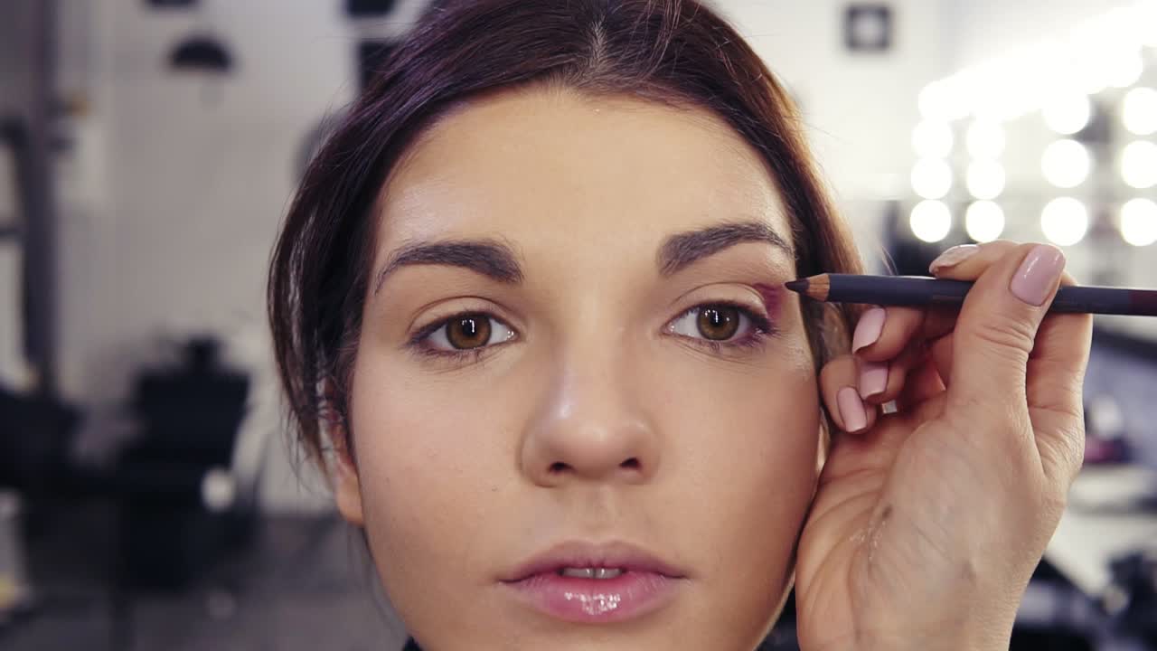 proceso de llenar la esquina exterior y el pliegue con delineador de ojos púrpura. hermosa chica de aspecto caucásico obtener un aspecto de maquillaje impecable hecho por un maquillador en el estudio de belleza.
