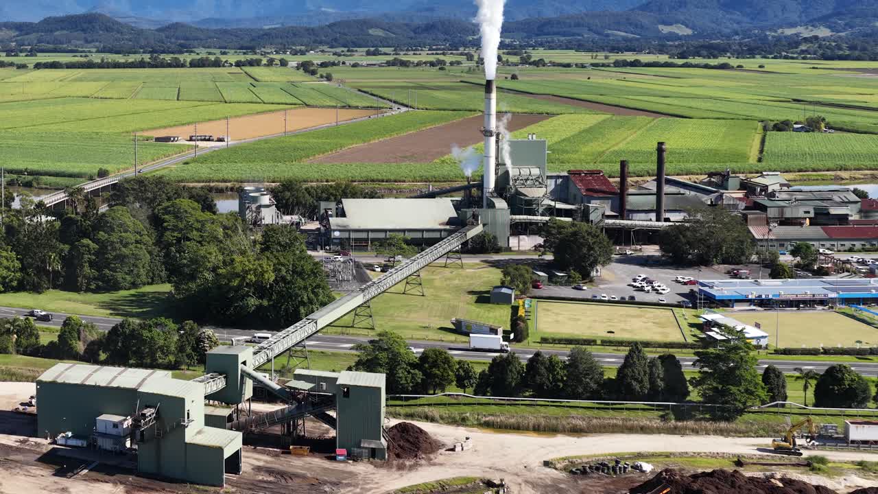 Aerial footage of a sugar mill surrounded by lush fields under clear skies, showcasing industrial and rural landscapes