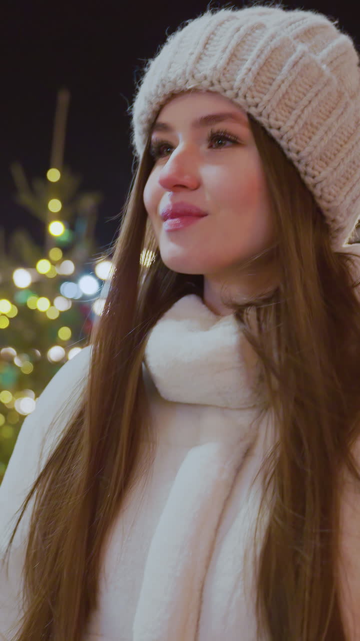 Woman in cozy winter outfit strolling outdoors at night, surrounded by twinkling festive lights, Christmas decorations, and people in the background