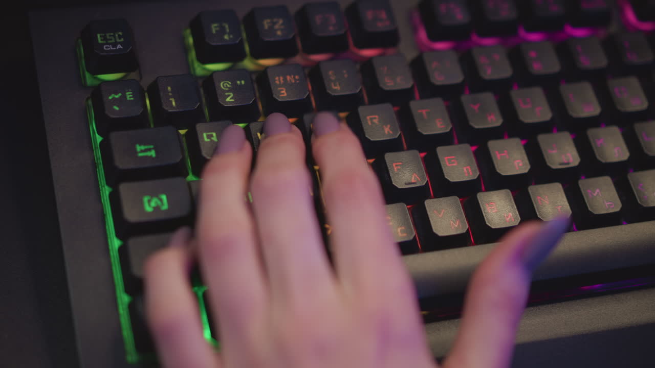 close up hand view of lady in fluffy sweater typing on rgb mechanical keyboard with glowing backlit keys and polished nails in cozy tech setup under ambient colorful lighting