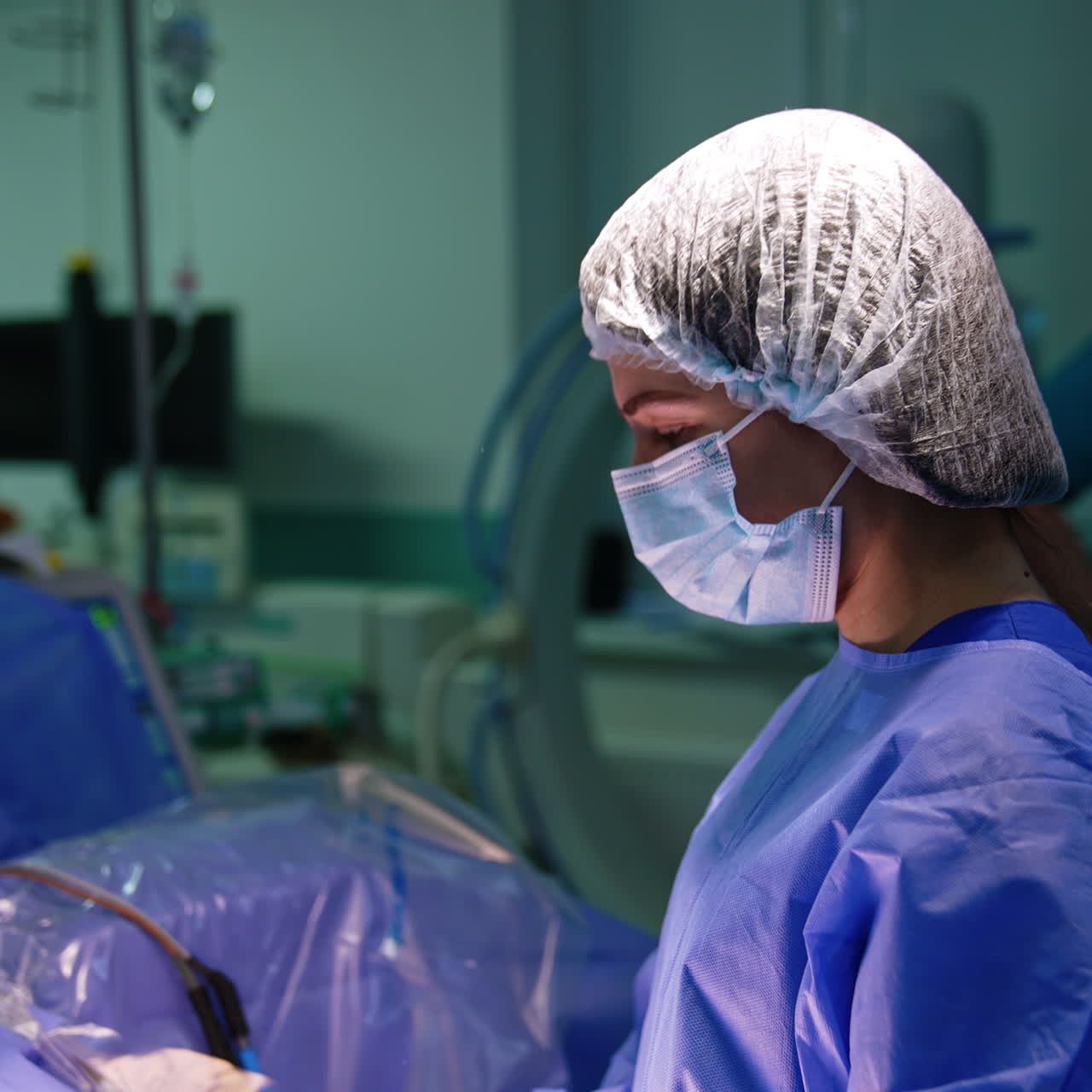 Female doctor in uniform, cap and mask stands in the surgery room. Side view of the medic prepared for operation.