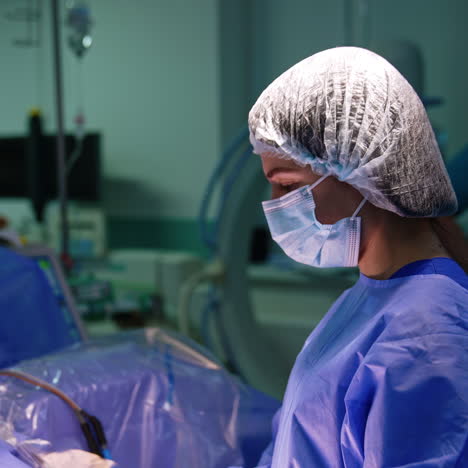 female doctor in uniform, cap and mask stands in the surgery room. side view of the medic prepared for operation.