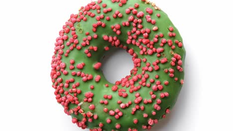 closeup fresh homemade doughnut with green glaze and pink sprinkle rotating isolated on white