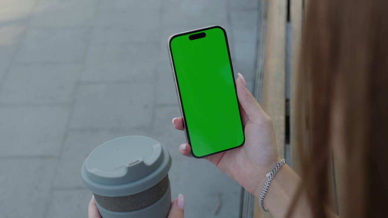 Woman holding phone with green screen and reusable cup