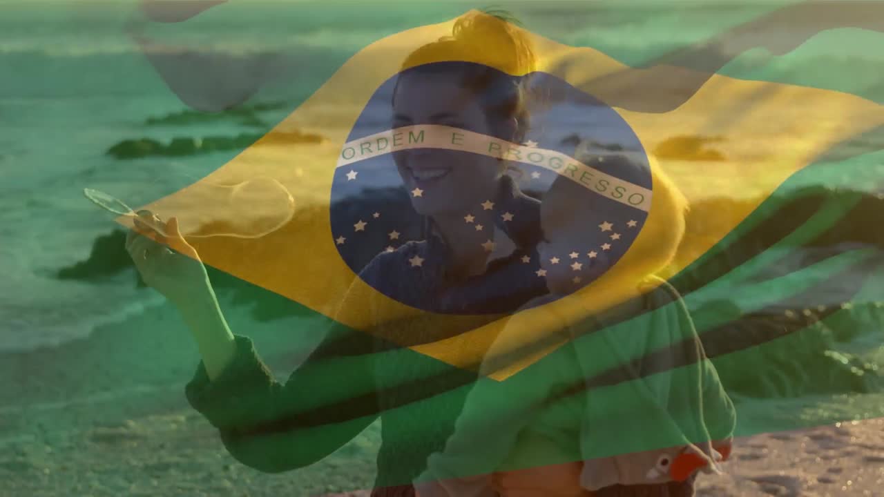 animación de la bandera de brasil sobre una madre caucásica feliz con un niño soplando burbujas en la playa