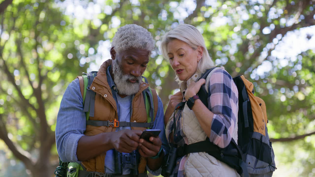 Senior Couple Hiking in Nature with Backpacks and Using a Phone