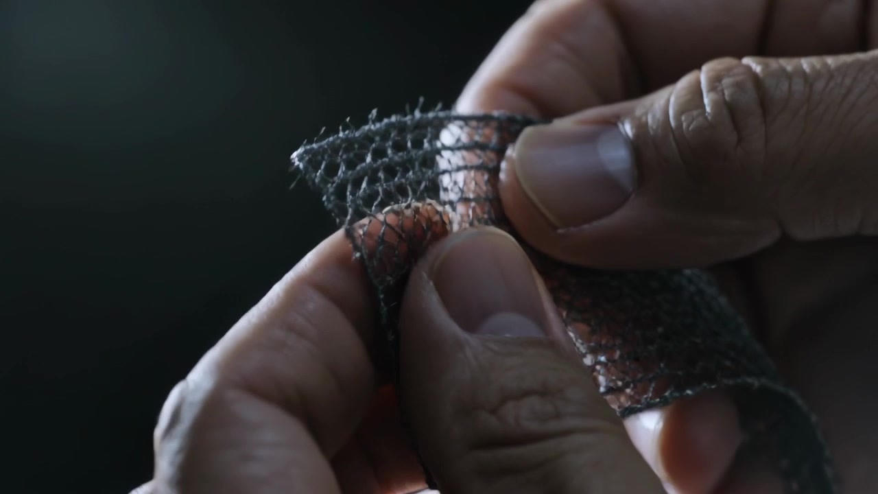 Männliche Hände begutachten Netzstoff in einem schwach beleuchteten Studio, wobei die Textur durch weiche Seitenbeleuchtung hervorgehoben wird