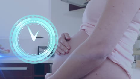 reloj con manecillas que se mueven rápidamente sobre una mujer caucásica embarazada feliz en la cocina masajeando el vientre