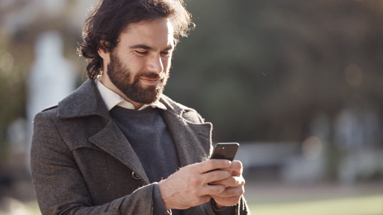 hombre emocionado enviando mensajes de texto en un teléfono afuera en un resfriado