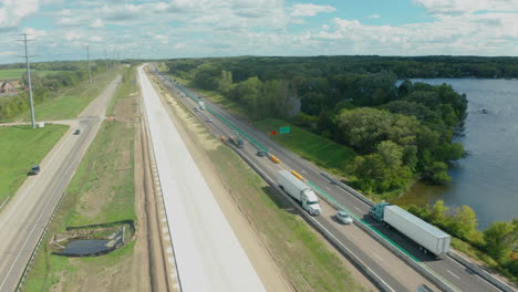 Vista-Aérea-Sobre-Una-Carretera-Muy-Transitada-Al-Lado-De-Una-Gran-Masa-De-Agua