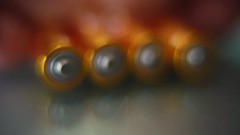 macro video of a pile of rolling batteries on a desk with reflection, golden battery, slow motion 120 fps, full hd, push in smooth movement