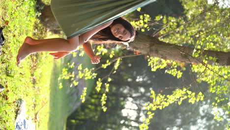 mujer de pelo largo y negro disfrutando de la vida en su hamaca en el parque natural durante un día soleado de camping