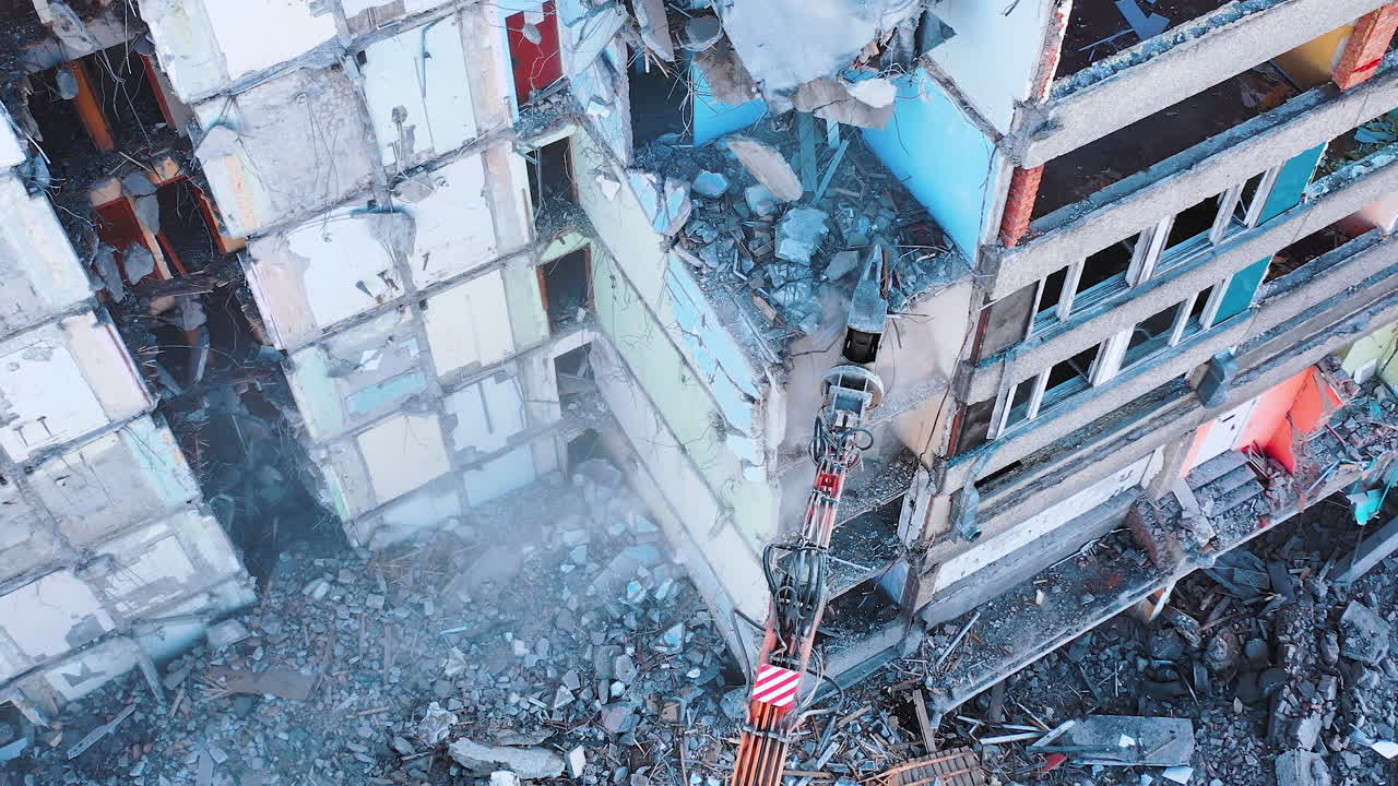 Demolishing vehicle breaks and throws down the parts of ruined house. Dismantling the old building with the help of machinery. View from above.