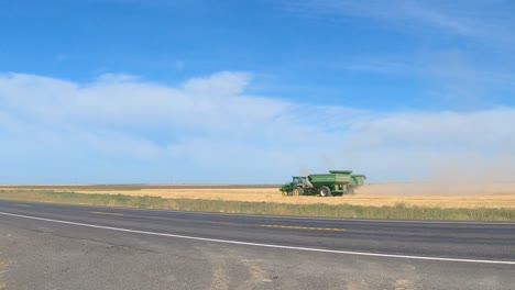 Combine-harvester-and-grain-wagon-are-harvesting-wheat-in-eastern-Washington-state-with-traffic-passing-in-the-foreground