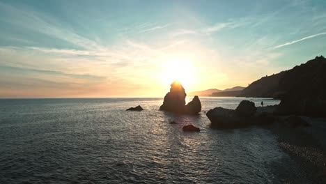 Felsensilhouette,-Antenne,-Die-Sich-Während-Des-Sonnenuntergangs-Am-Strand-Rückwärts-Bewegt