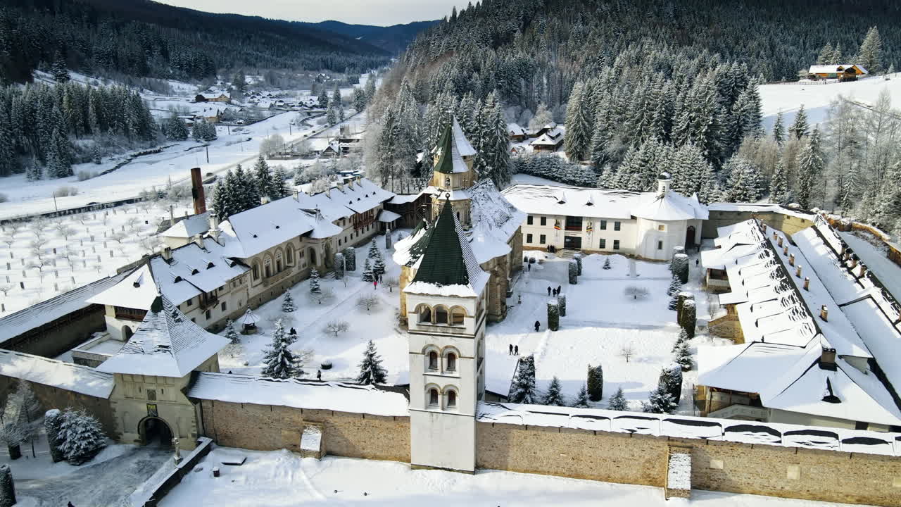 Lotniczy widok z drona na monastyr Putna zimą, Rumunia. Wewnętrzny dziedziniec z przechadzającymi się turystami, nagie drzewa, śnieg, wzgórza wokół