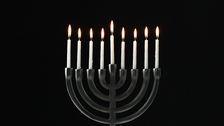 A row of nine white candles burning in a menorah are blown out, front view