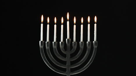 a row of nine white candles burning in a menorah are blown out, front view