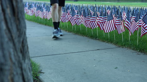 legs of a person walking in the park passing by american flags on stick standing on the grass