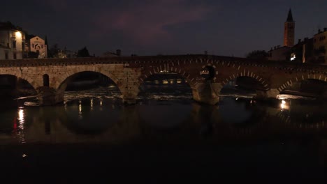 imagen aérea de un dron pasando por el puente ponte pietra en verona por la noche cerca del río adige