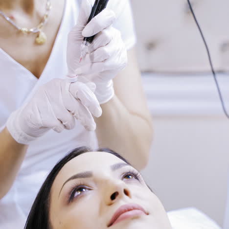 skilled beautician fiiling up tattoer machine with red ink to make permanent make-up. cosmetologist preparing for procedure of permanent make-up on lips for a young female in a beauty salon.
