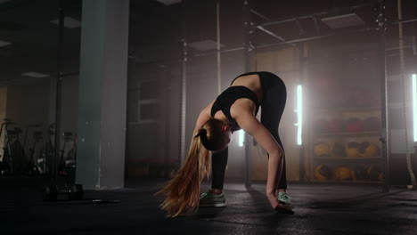 a young slender woman prepares and warms up before training. hitching and stretching muscles after a tedious hard workout in the dark interior of the fitness room