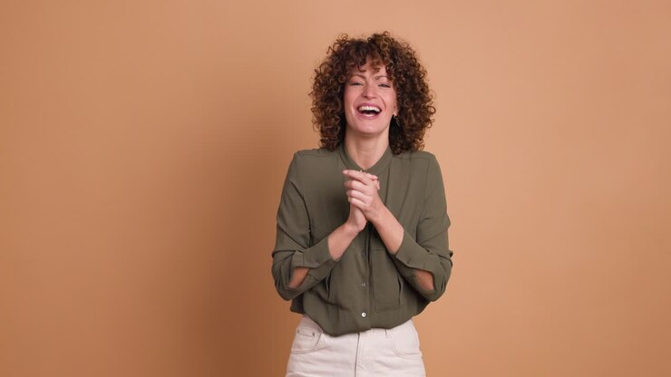 Giovane donna entusiasta che batte le mani e sorride su sfondo beige