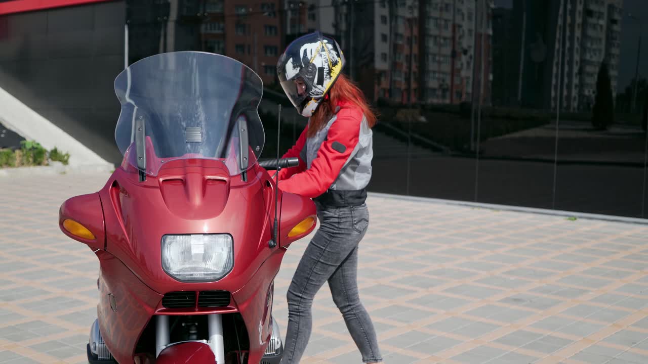 Girl biker mounts motorcycle. Female biker sitting on a motorcycle, putting on protective helmet