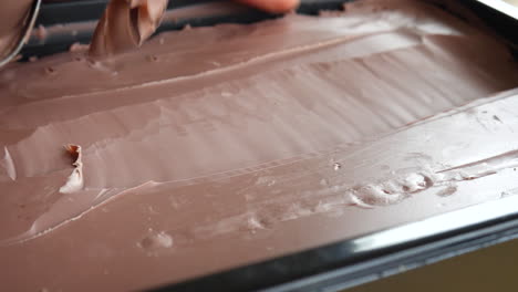 an artist in a studio carving brown modeling clay from a large block with a hand tool in a satisfying shaving to start his art sculpting