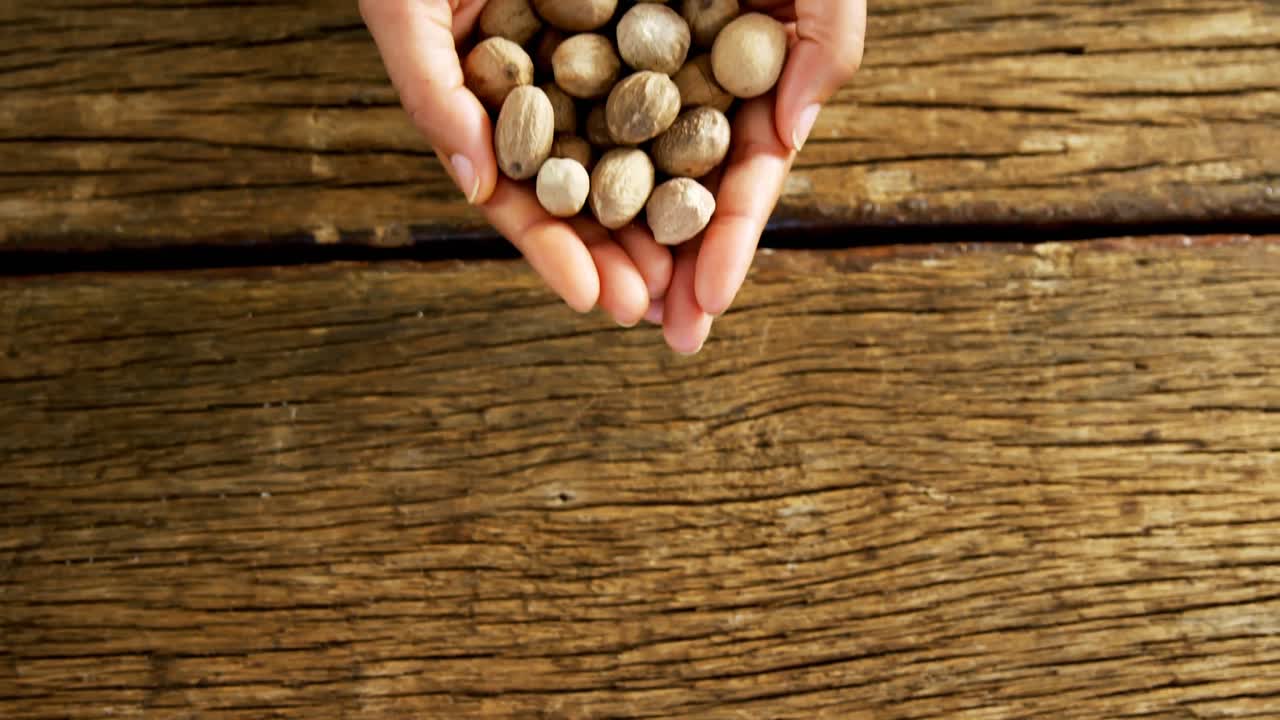 Hands of woman holding nutmeg over wooden platform 4k