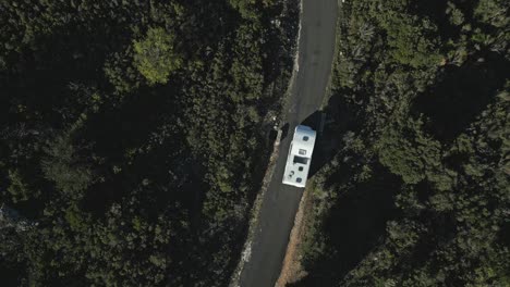 Bird's-eye-view-of-white-camper-van-travelling-along-narrow-winding-road