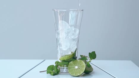 glass with lime and ice cubes stands on white table at wall