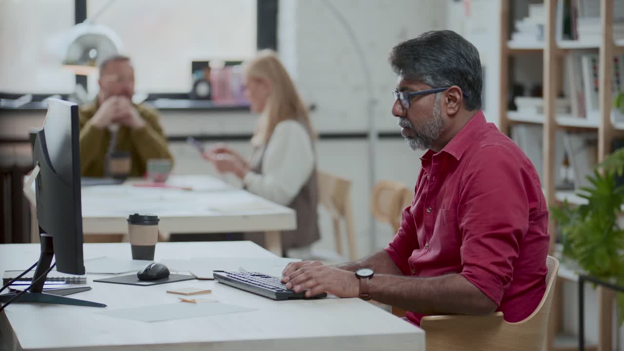 Indian Businessman Typing on Computer and Making Notes at Office Desk