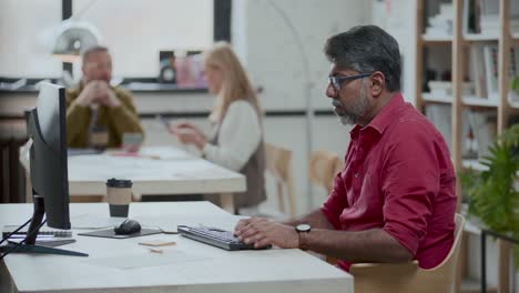 indian businessman typing on computer and making notes at office desk