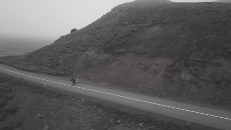 Drohnenaufnahmen-Von-Skatern,-Die-Auf-Kurvigen-Straßen-In-Einer-Nebligen,-Dramatischen-Landschaft-In-Island-Bergab-Fahren