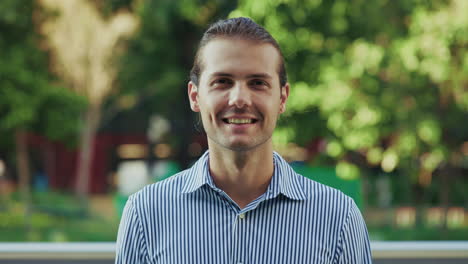 a smiling young man in a striped shirt looking at the camera outdoors