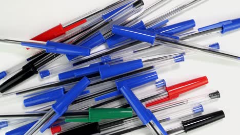 a lot of colorful ballpoint pens spinning rotate slowly on white screen in office or school.