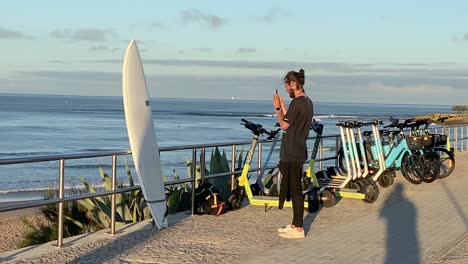 Viajero-Masculino-En-Traje-Toma-Fotos-Panorámicas-De-Su-Increíble-Nueva-Tabla-De-Surf-Muy-Orgulloso