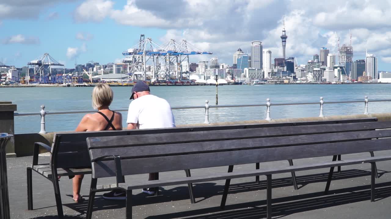 SLOWMO - Older couple sitting on bench in Devonport harbour and looking at Auckland skyline, New Zealand